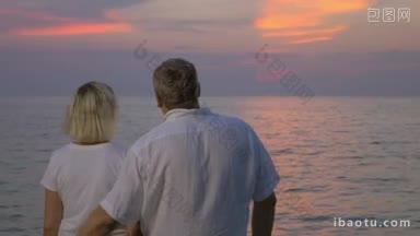 慢动作的老年夫妇拥抱在一起，享受美丽的海景和日落的背影